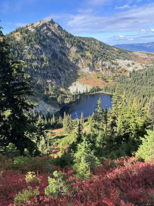 A scenic view of a mountain landscape with a lake surrounded by trees and colorful autumn foliage.