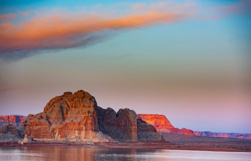 A serene landscape featuring colorful rock formations and a calm body of water under a pastel sky at sunset.