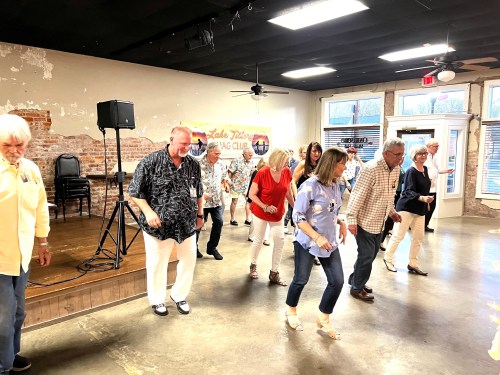 A group of people dancing in a spacious venue with a rustic interior, enjoying a lively event.