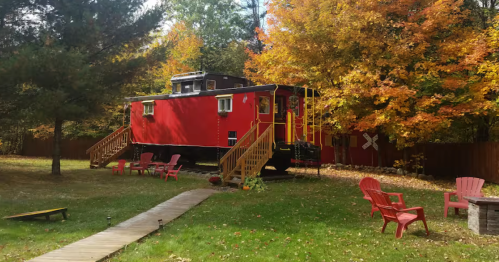 A red train caboose Airbnb surrounded by vibrant autumn fall foliage and lawn chairs in New Hampshire.