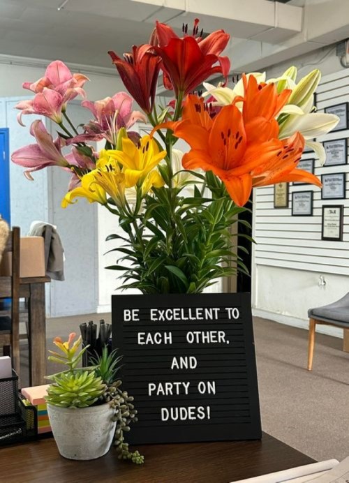A vibrant bouquet of lilies beside a sign that reads, "Be excellent to each other and party on dudes!"