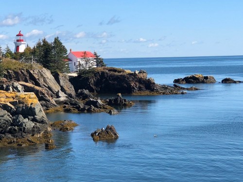 A serene coastal scene featuring a lighthouse, rocky shore, and calm blue waters under a clear sky.