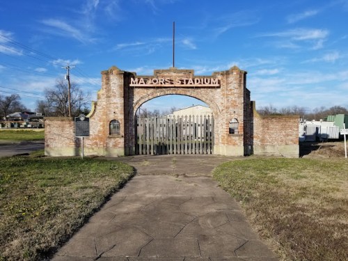Entrance to Mayor's Stadium, featuring a brick archway and wooden gates, set against a clear blue sky.