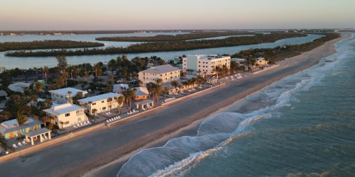 Aerial view of a beachside resort with palm trees, sandy shore, and calm waters at sunset.