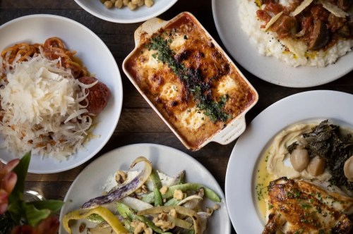 A variety of dishes including pasta, baked casserole, rice, and vegetables arranged on a wooden table.