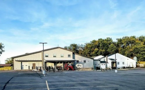 A large metal building with a tractor parked outside, surrounded by trees and a clear blue sky.