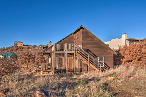 A wooden cabin with a deck, surrounded by dry grass and trees, under a clear blue sky.