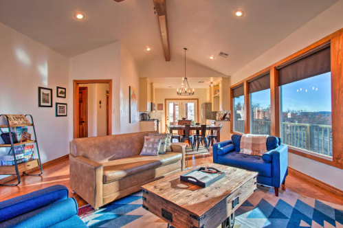 Cozy living room with blue and brown sofas, a wooden coffee table, and large windows overlooking a scenic view.