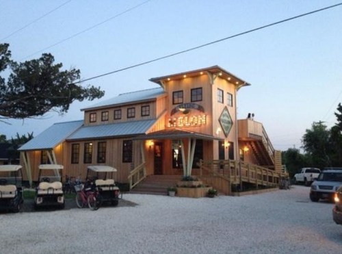 A wooden building with a lit sign, surrounded by golf carts and trees, at dusk.