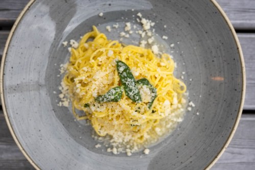 A bowl of pasta topped with grated cheese and green herbs, served on a textured gray plate.