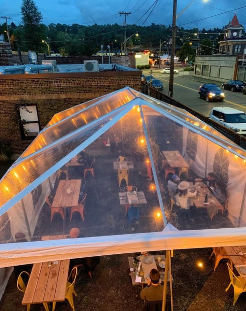 A cozy outdoor dining area under a clear tent, with string lights and tables filled with diners at dusk.