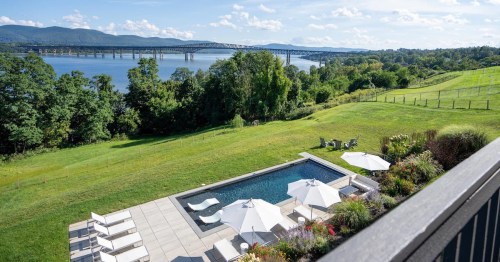 A scenic view of a poolside area with umbrellas, overlooking a river and bridge, surrounded by lush greenery.