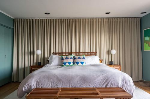 A cozy bedroom featuring a wooden bed with colorful pillows, bedside lamps, and soft curtains in calming colors.