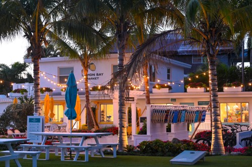A charming beachside market with palm trees, string lights, and colorful umbrellas at dusk.
