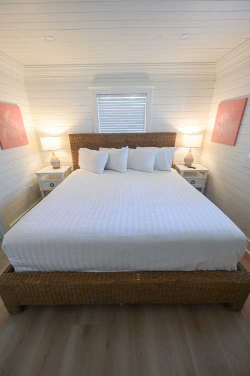 A cozy bedroom featuring a woven bed frame, white bedding, and two bedside lamps with pink artwork on the walls.