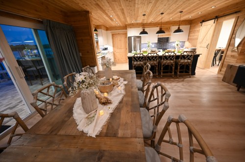 A cozy wooden dining area with a large table, decorative centerpieces, and a view of a modern kitchen.