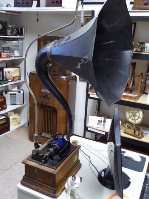 A vintage gramophone with a large horn, wooden base, and a small dog figurine beside it, displayed in a museum.