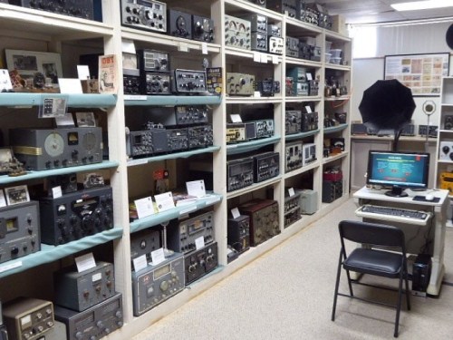 A room filled with vintage radios and audio equipment, with a computer setup on a desk in front.