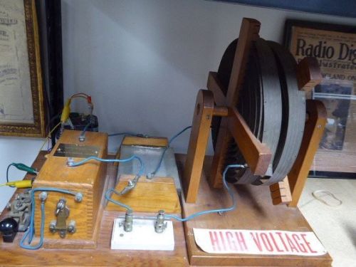 A vintage high voltage generator with wooden components and wires, featuring a large reel and control panel.