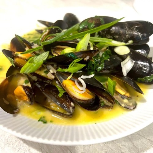 A plate of mussels cooked in a flavorful broth, garnished with green onions and herbs.