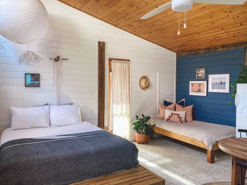 Cozy bedroom with a bed, daybed, plants, and decorative wall art in a bright, airy space.