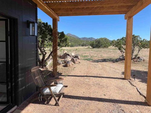 A wooden chair on a porch overlooking a rocky path and open landscape with distant mountains under a clear blue sky.