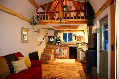 Cozy interior of a rustic cabin with a loft, wooden accents, a kitchen, and a red sofa. Warm and inviting atmosphere.