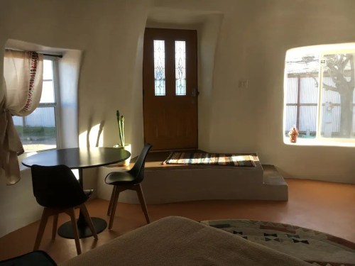 Cozy interior of a minimalist room with a round table, chairs, and a welcoming entrance with natural light.