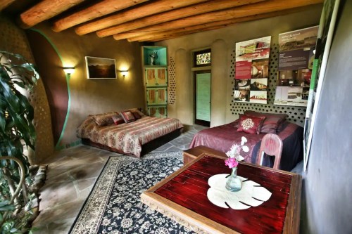 Cozy room with two beds, wooden beams, a decorative rug, and a small table with a vase of flowers.