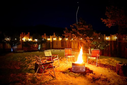A cozy outdoor fire pit surrounded by chairs, illuminated by warm flames against a night sky.