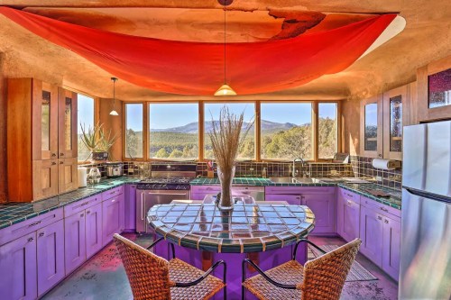 Bright kitchen with purple tile, large windows showcasing a mountain view, and a red fabric draped overhead.