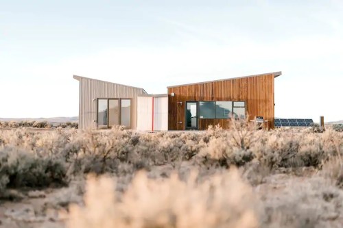 Modern house with a mix of wood and metal exterior, set in a desert landscape with sparse vegetation.