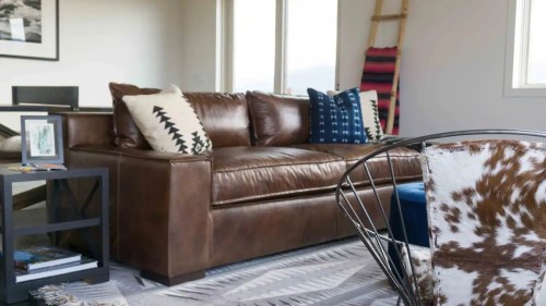 A cozy living room featuring a brown leather sofa with decorative pillows, a patterned rug, and stylish furniture.
