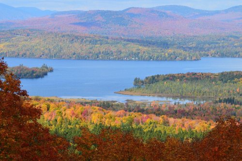 A scenic view of a lake surrounded by vibrant autumn foliage and rolling hills in the background.