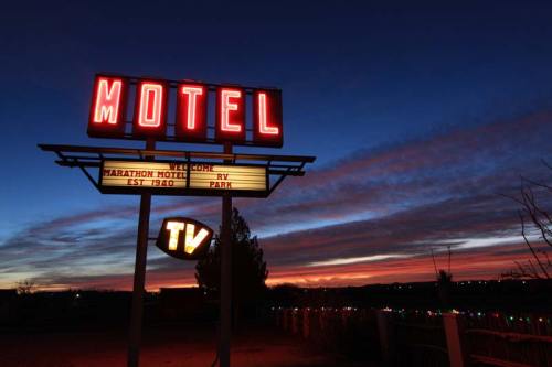 Neon motel sign at sunset, with "Marathon Motel RV Park" and "TV" illuminated against a colorful sky.