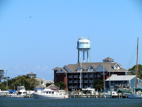 Ocracoke water tower beside a marina with boats and a clear blue sky in the background.