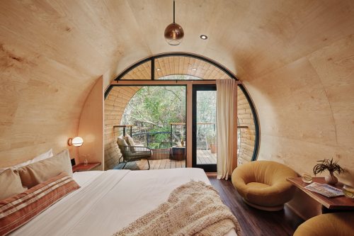 Cozy, modern bedroom with wooden walls, large windows, and a balcony overlooking lush greenery.