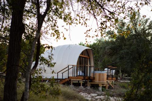 A modern, curved cabin nestled among trees, featuring a wooden deck and hot tub, surrounded by nature.