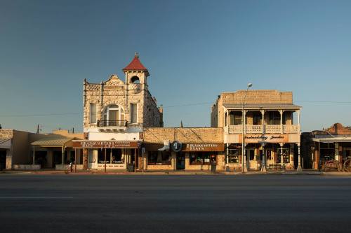 Historic buildings line a street, featuring unique architecture and storefronts under a clear blue sky.