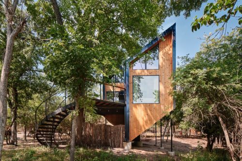 A modern treehouse with a spiral staircase, surrounded by trees and featuring large windows.