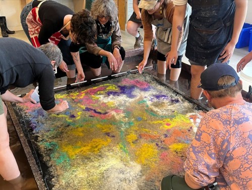 A group of people creating colorful art on a large, wet surface, using various materials and techniques.