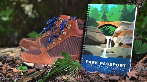 A pair of hiking boots next to an Ohio State Parks passport guidebook on a forest floor.