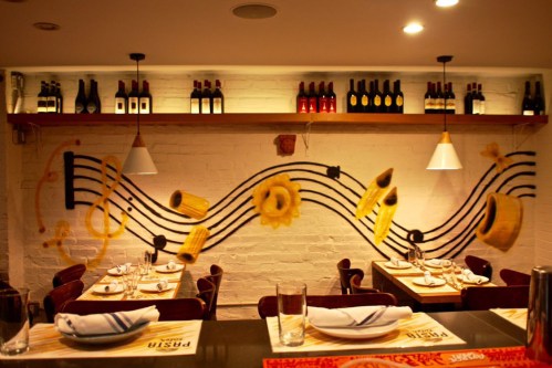 A cozy restaurant interior featuring a musical note mural and shelves of wine bottles above dining tables.