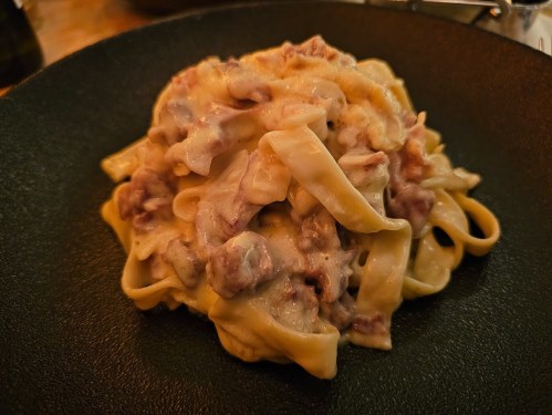 A plate of creamy pasta with strips of fettuccine and chunks of meat, served on a dark plate.