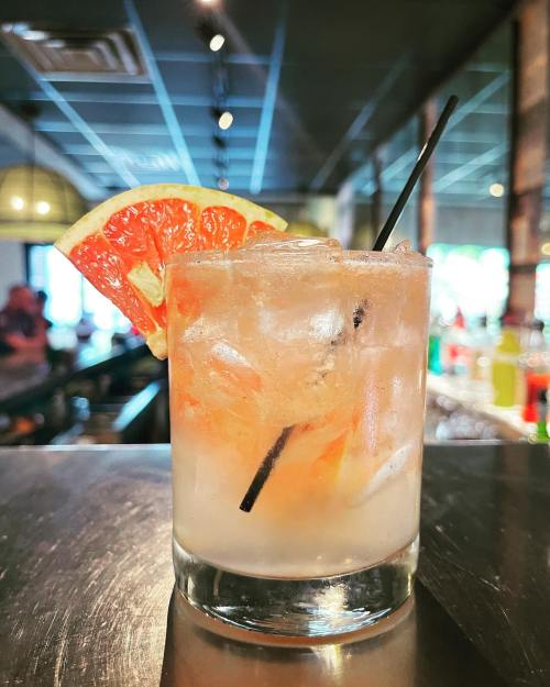 A refreshing cocktail with ice, garnished with a slice of grapefruit, served in a clear glass on a bar counter.