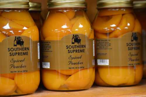 Jars of Southern Supreme spiced peaches lined up on a shelf, showcasing bright orange fruit in syrup.