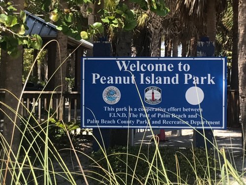 Sign welcoming visitors to Peanut Island Park, featuring logos of local organizations and surrounded by greenery.