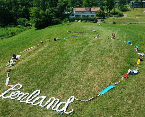 Aerial view of a grassy field with people lying around the word "Penland" formed by colorful objects.