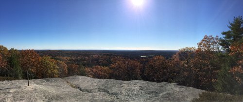Panoramic view of a vibrant autumn landscape with colorful trees and a clear blue sky. Sun shining brightly above.