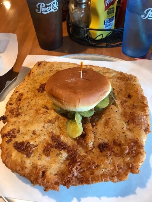 A large, crispy fried chicken sandwich on a giant, golden-brown breaded patty, topped with pickles and a bun.